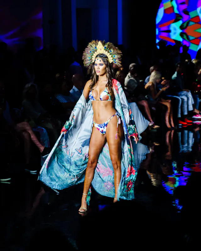 Luxeisle runway model wearing a floral bikini and flowing botanical-print robe with a peacock-feather headpiece