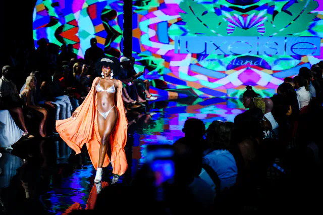 Model in a silver bikini and orange robe walking beneath a colorful Luxeisle backdrop